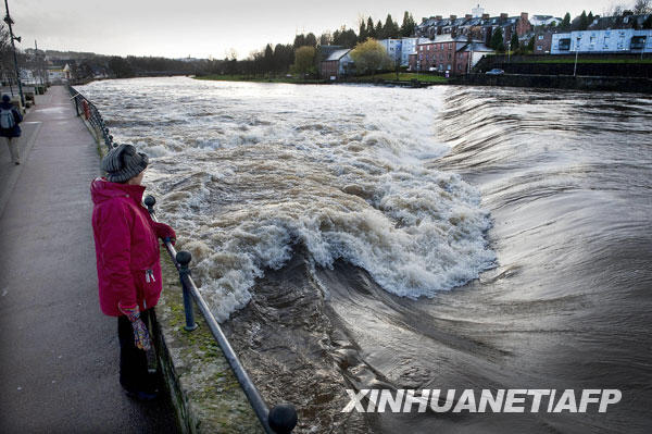 11月22日，在苏格兰西南部邓弗里斯，一名妇女看着泛滥的尼思河。连续的暴雨导致英国西北部地区一些河流水位上升，引发洪水警报。